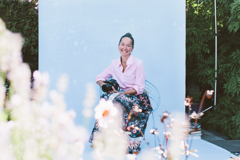 Gina holding a camera in front of a studio backdrop in a garden